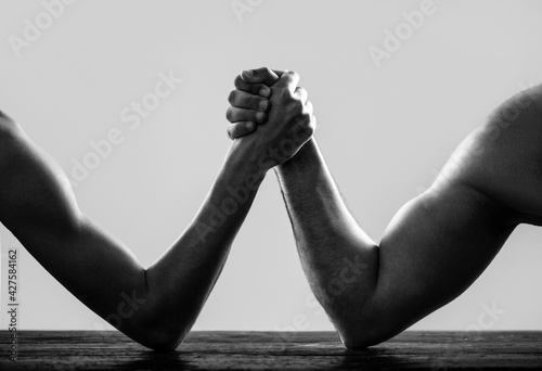 Arms wrestling thin hand and a big strong arm in studio. Arm wrestling. Heavily muscled man arm wrestling a puny weak man. Two man's hands clasped arm wrestling, strong and weak. Black and white