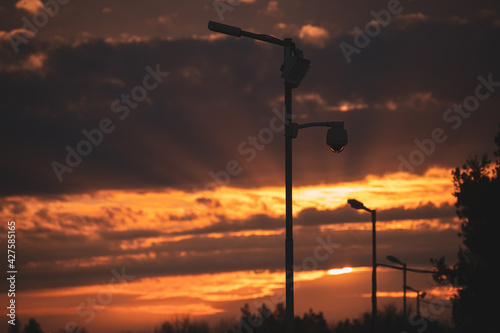 Surveillance camera silhouette. Dramatic sunset sky in background. Security technology.
