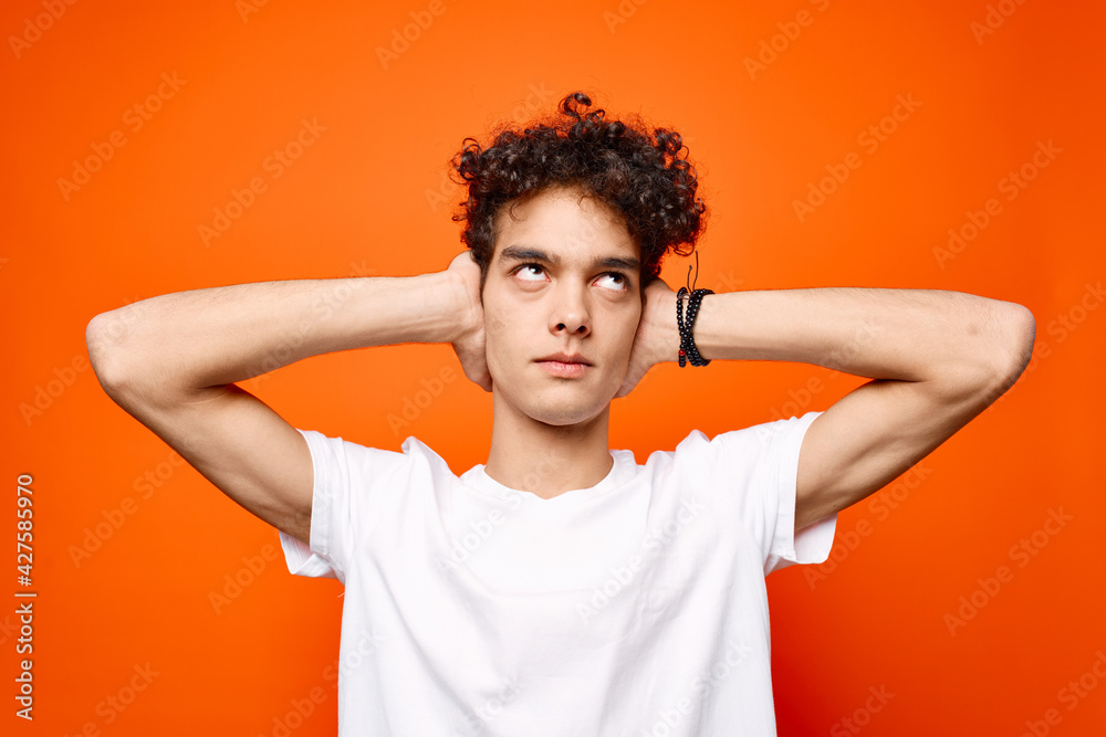 guy in a white t-shirt with curly hair holding his head emotions orange background guy in a white t-shirt with curly hair holding his head emotions orange background