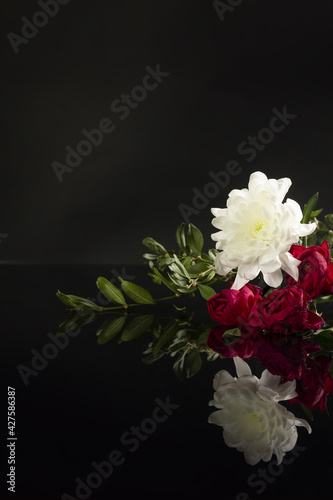 Beautiful bouquet of flowers: red roses, white chrysanthemums, green leaves on black background