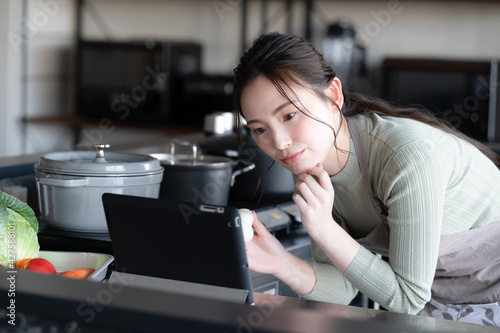 の料理にしようかタブレットでレシピを選んで微笑む美人な日本人女性 正面コピースペースあり