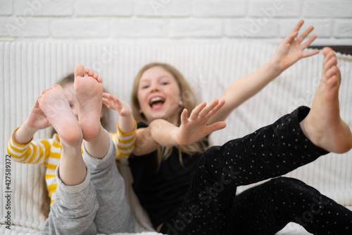 two happy Caucasian girls playing around on the couch at home, having fun and laughing. Children's feet and hands close-up. The concept of a happy childhood, holidays and entertainment.