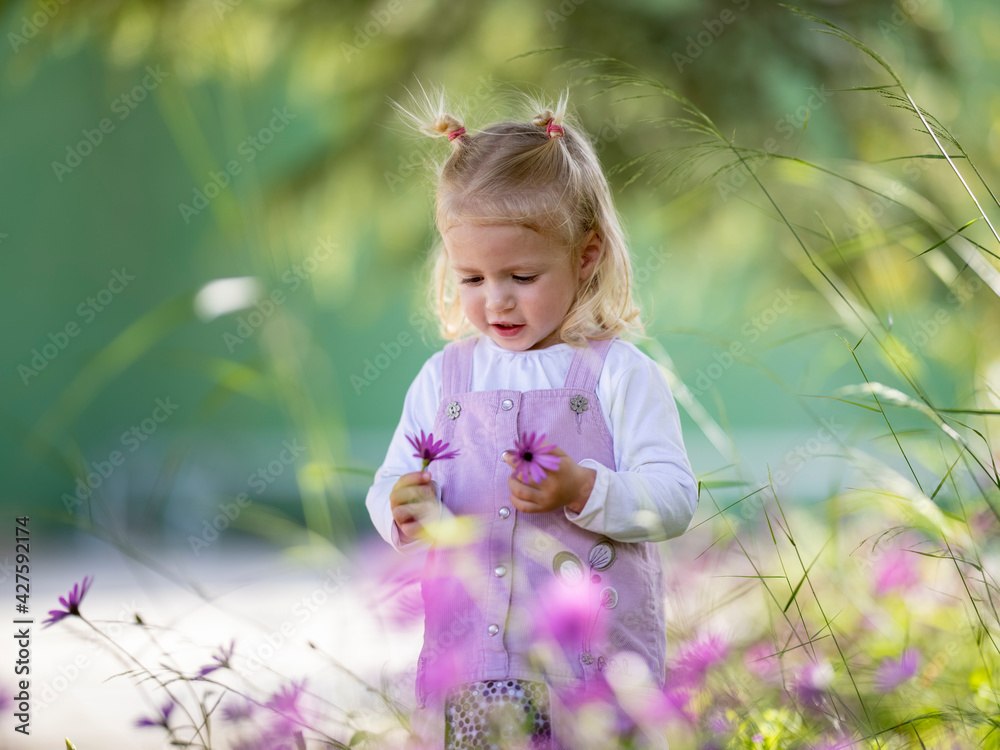 Adorable niña rubia de año y medio recogiendo flores