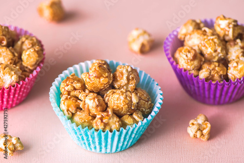 Sweet caramel popcorn in a colorful cups on a pink background