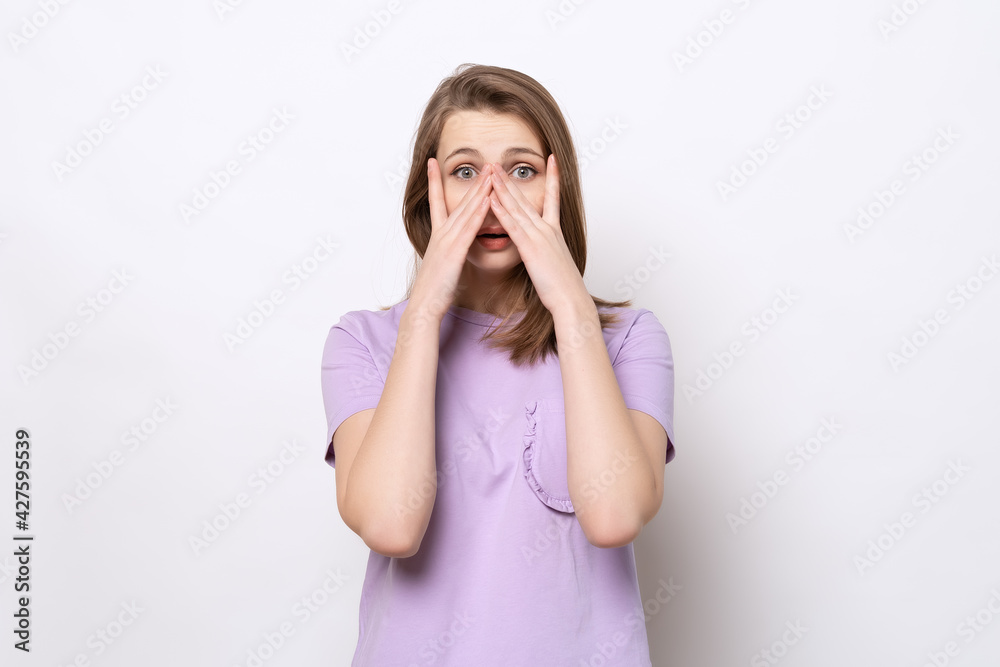 scared girl hiding face in palms hands and peering out with one eye between her fingers, trembling fear scared girl hiding face in palms hands and peering out with one eye between her fingers, trembling fear