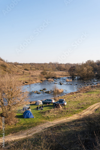 Distance view. Copy space. Morning landscape with a tents and 4wd cars, the river bank and rocks in the background. Spring camping. Tourism and vacation. Vertical photo