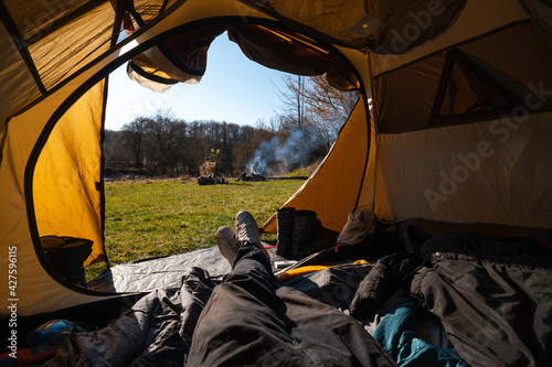 First-person view from the tent. Male feet. View of the grass, fire and river. Tourism and recreation concept. Tourist equipment.
