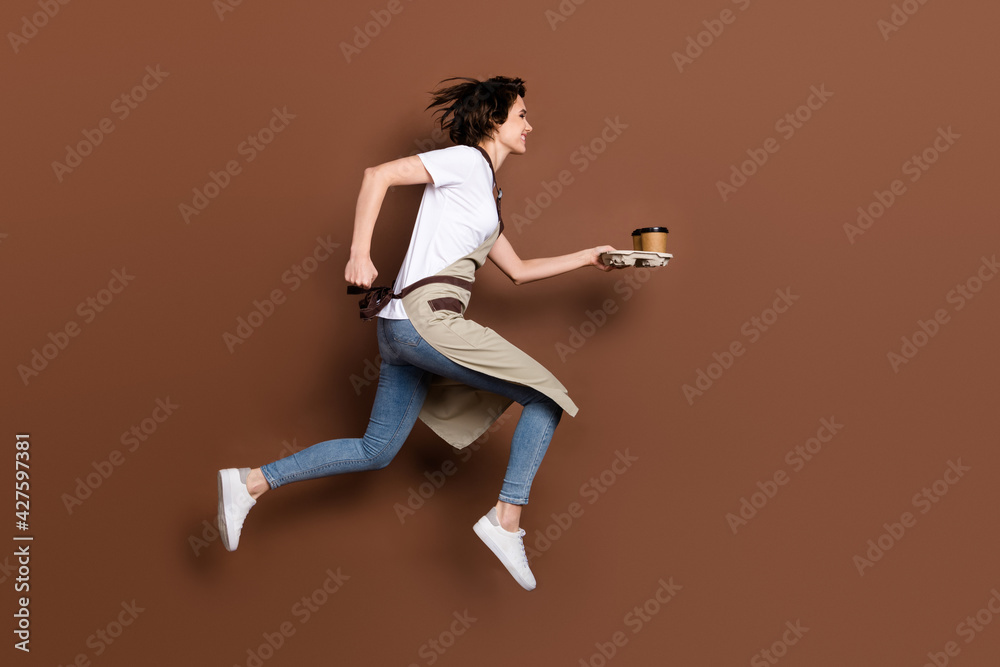 Full size profile side photo of happy cheerful woman barista running with coffee look copyspace isolated on brown color background