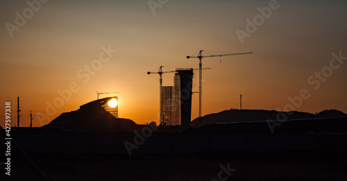 Construction of modern high-rise ski-jump in Shchuchinsk city, Kazakhstan. Silhouette of tower and sun disk on sunset or sunrise. Warm tones. photo