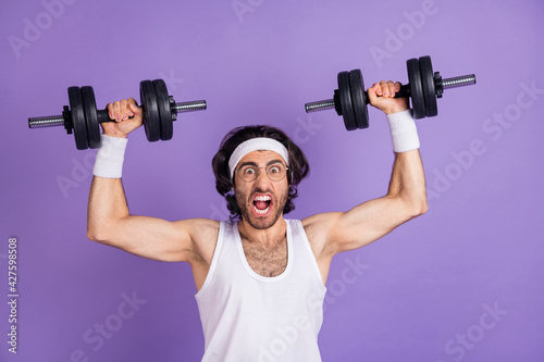 Photo of crazy sportsman raise hands hold dumbbells open mouth wear glasses singlet isolated purple background