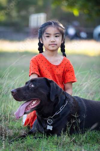A young girl in red outfits plays with her big black dog in the backyard in the evening with her family