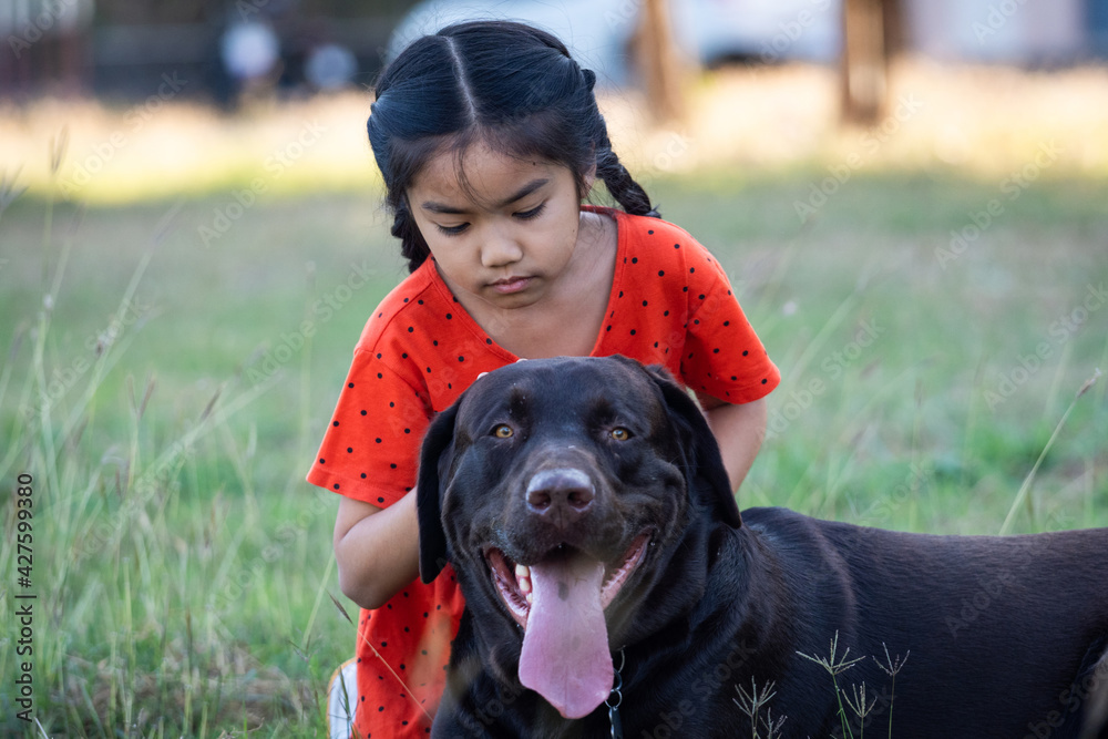 A young girl in red outfits plays with her big black dog in the backyard in the evening with her family A young girl in red outfits plays with her big black dog in the backyard in the evening with her family