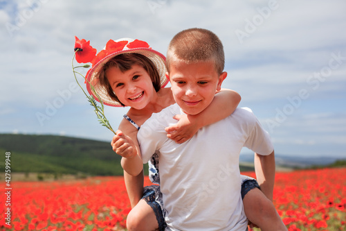The boy and girl have fun in the field with red flowers. Child relax and enjoy the summer vacation. First love