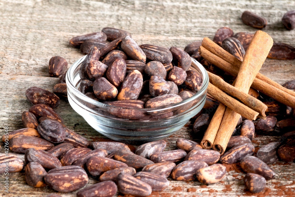 Fototapeta premium Cocoa beans in a glass bowl on a wooden background and sprinkled on the floor