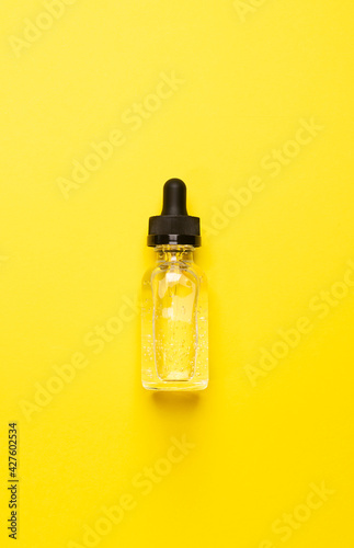 Cosmetic liquid gel serum lubricant in a transparent glass bottle with a dropper pipette on a yellow background