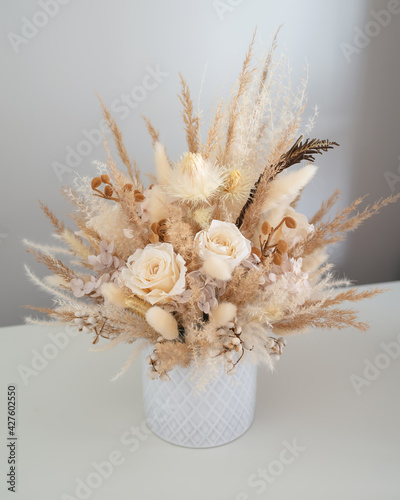 Stylish composition of stabilized flowers and dried flowers in light colors on a light background. Photo of a bouquet with roses in a vase. Close-up color photo.