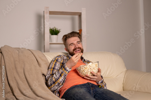 Bearded man watching film or sport games TV eating popcorn in house at night. Cinema, championship and fan concept.