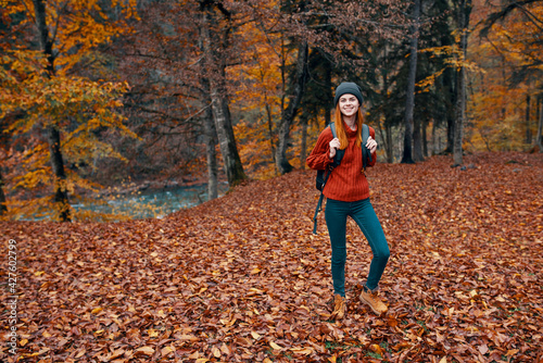 travel tourism and a young woman with a backpack walks in the park in nature landscape tall trees fallen leaves river