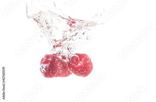 Raspberries splashing in water on white
