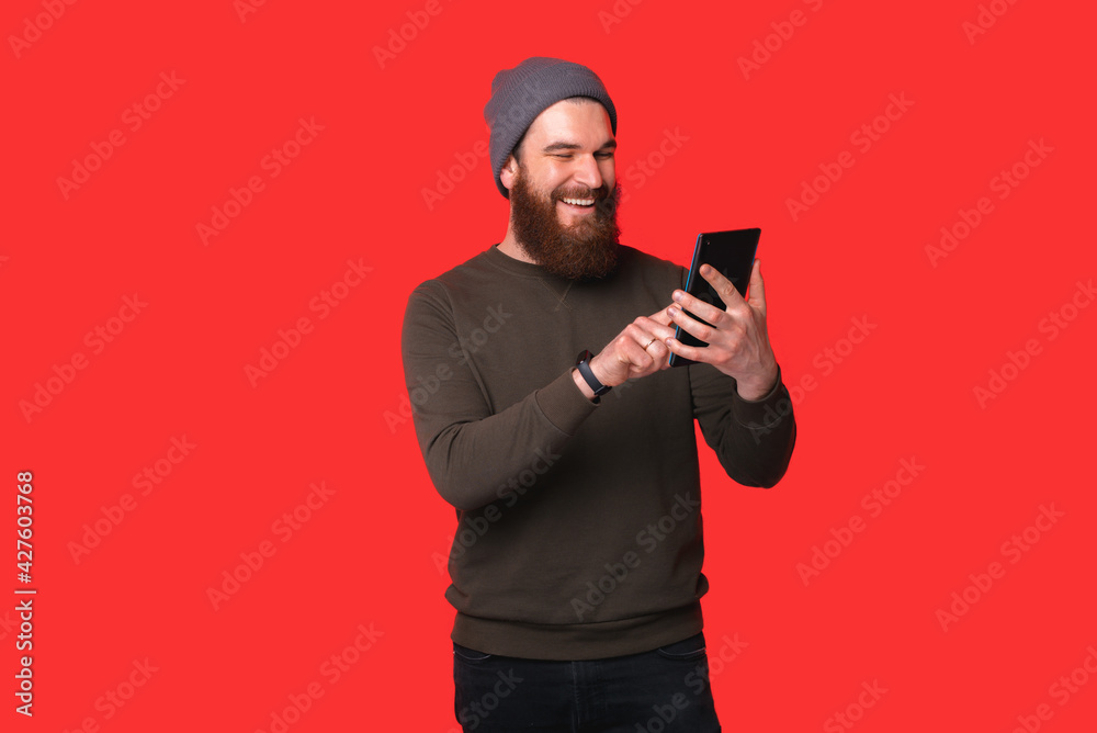 Cheerful young bearded hipster man using tablet over red background Cheerful young bearded hipster man using tablet over red background