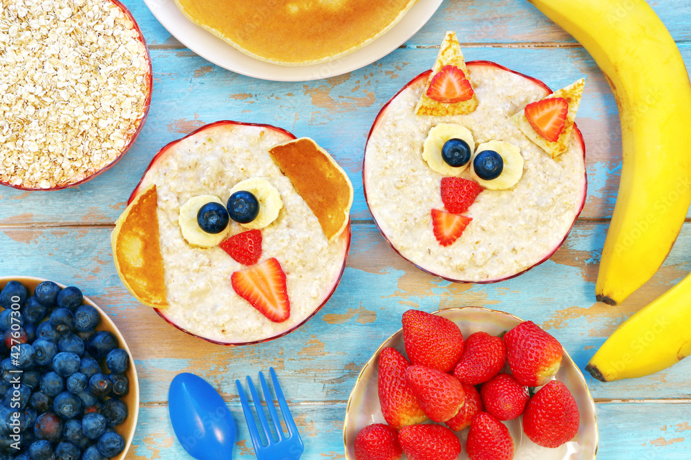 Obraz premium Creative idea for kids breakfast. Cute oatmeal cat and dog with berries on blue wooden table, top view. Healthy vegetarian eating for children