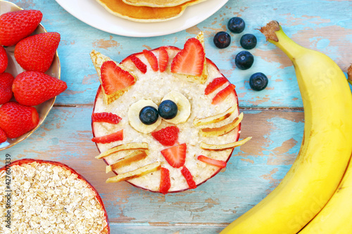 Fun food for kids - cute oatmeal cat tiger on blue wooden table, top view. Healthy vegetarian eating for children