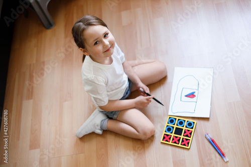 Little girl draws tic-tac-toe while sitting on the floor at home
