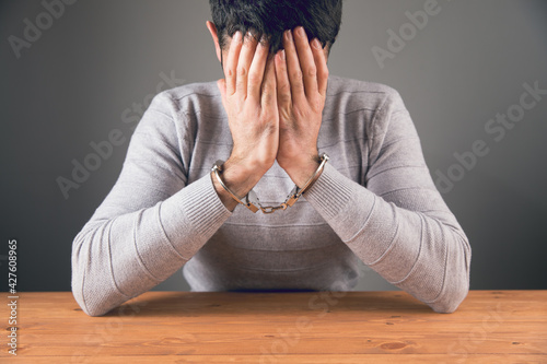 Fotografie sitting in handcuffs covering his face