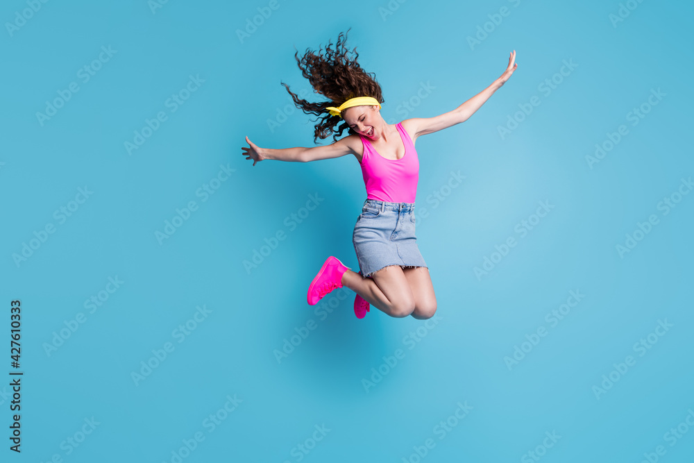 Photo of impressed sweet young lady wear pink singlet jumping high arms sides isolated blue color background Photo of impressed sweet young lady wear pink singlet jumping high arms sides isolated blue color background