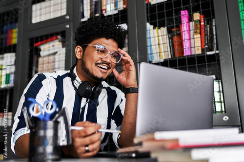 A smiling Indian teacher, a student at a computer, looks at a laptop, smiles and gives a lecture, distance learning