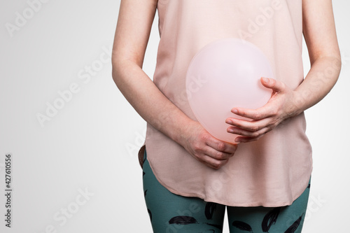 Woman pregnant or bloated belly. Pink balloon in woman's hands. Abstract background photo
