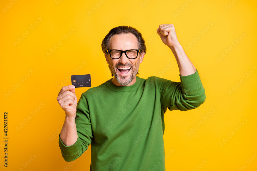 Photo of excited man presenting plastic debit card raise fist wear glasses green sweater isolated yellow color background Photo of excited man presenting plastic debit card raise fist wear glasses green sweater isolated yellow color background