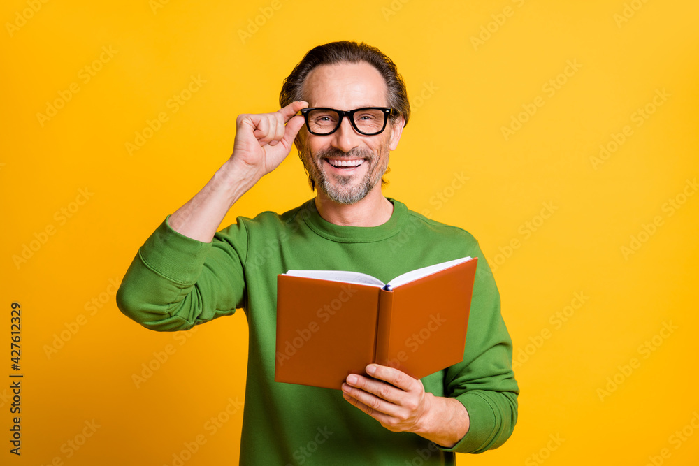 Photo of guy hold textbook look camera shiny smile wear green pullover isolated yellow color background Photo of guy hold textbook look camera shiny smile wear green pullover isolated yellow color background
