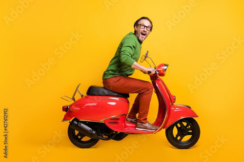 Photo of crazy man ride moped travel enjoy wear glasses green pullover pants footwear isolated yellow color background © deagreez