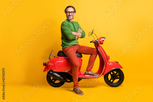 Photo of self-assured man ride moped crossed hands wear eyewear green sweater pants footwear isolated yellow color background © deagreez