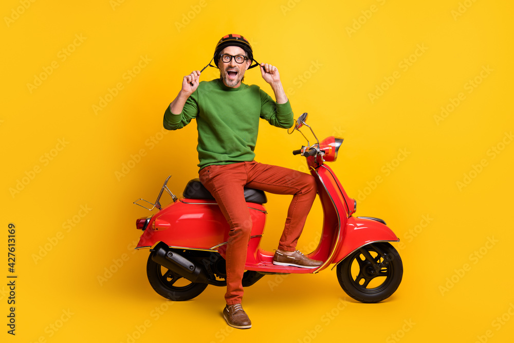 Photo of crazy guy on scooter open mouth wear helmet specs green sweater trousers isolated yellow color background