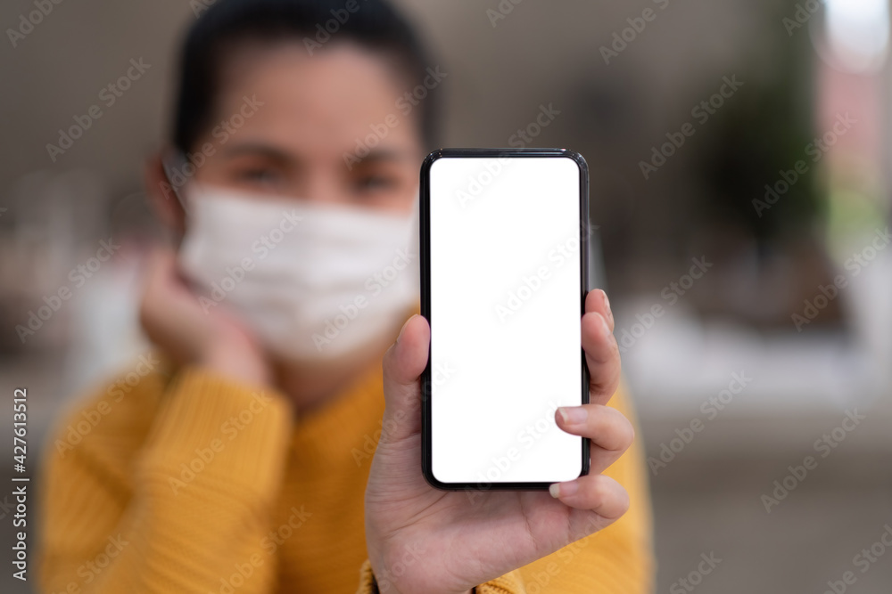 Mockup image of a beautiful woman wear mask while holding mobile phone with blank white screen.