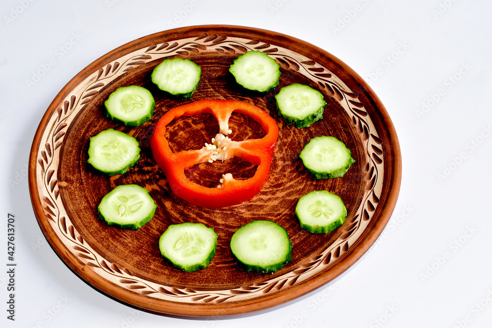 On the plate are red bell peppers and round green cucumber wedges. On the plate are red bell peppers and round green cucumber wedges.