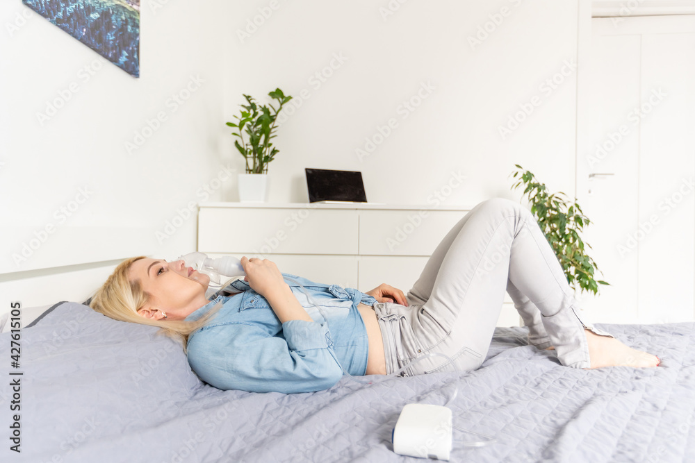 Sick beautiful female in blue cloth hold nasal mask with respiratory problem in hospital room. woman patient inhalation therapy by the mask of inhaler with soft stream smoke from bronchodilator. Sick beautiful female in blue cloth hold nasal mask with respiratory problem in hospital room. woman patient inhalation therapy by the mask of inhaler with soft stream smoke from bronchodilator.