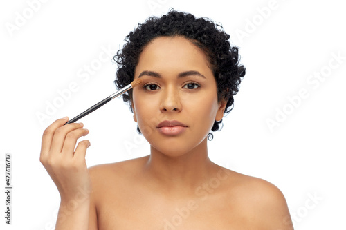 beauty, cosmetics and people concept - beautiful young african american woman with make up brush applying eye shadows over white background