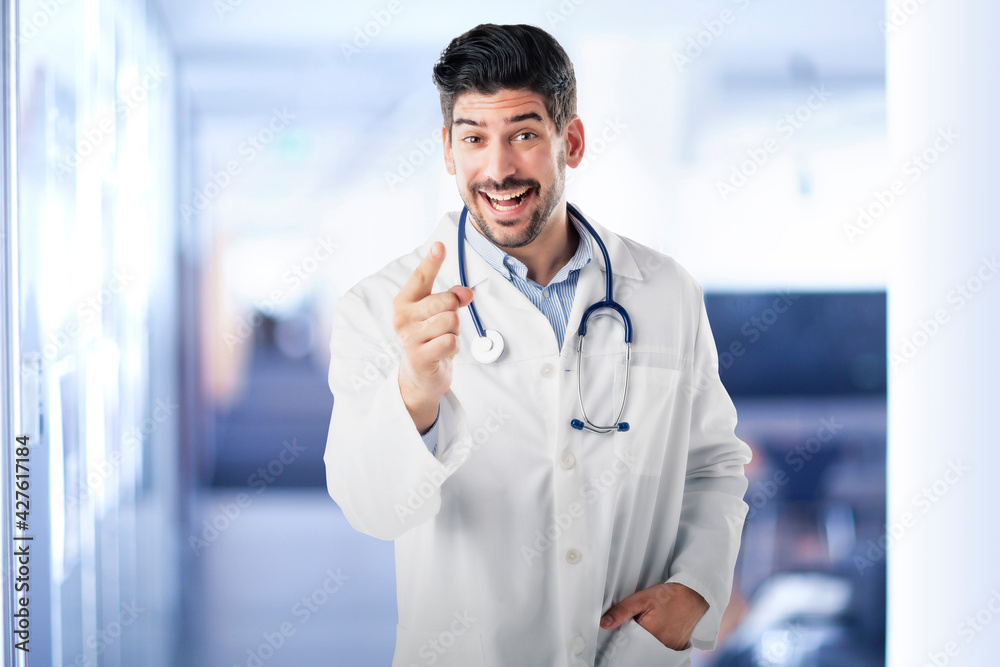 Happy male doctor pointing his finger to you while standing at clinic foyer Happy male doctor pointing his finger to you while standing at clinic foyer