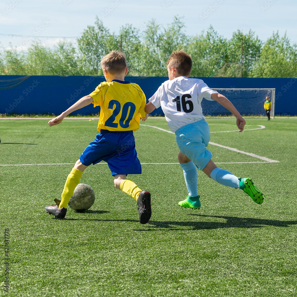 Obraz premium Children's football. An interesting football moment at the match and training. The active struggle and dynamics of the boys' soccer match. The boys are recklessly fighting for the ball