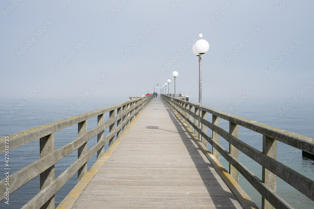Kuehlungsborn pier made of wood with lanterns and seagull on a sunny day with sea fog