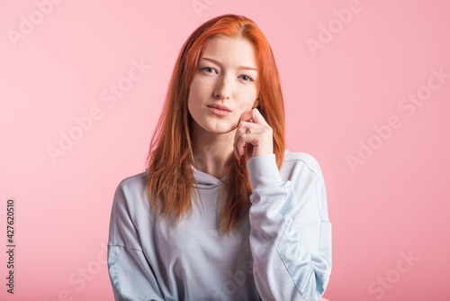 Portrait of a redhead pensive girl in the studio on a pink background