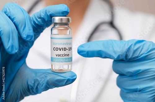 Doctor or laborant in protective gloves holding ampule tube with nCoV Coronavirus vaccine for COVID virus and finger pointing.