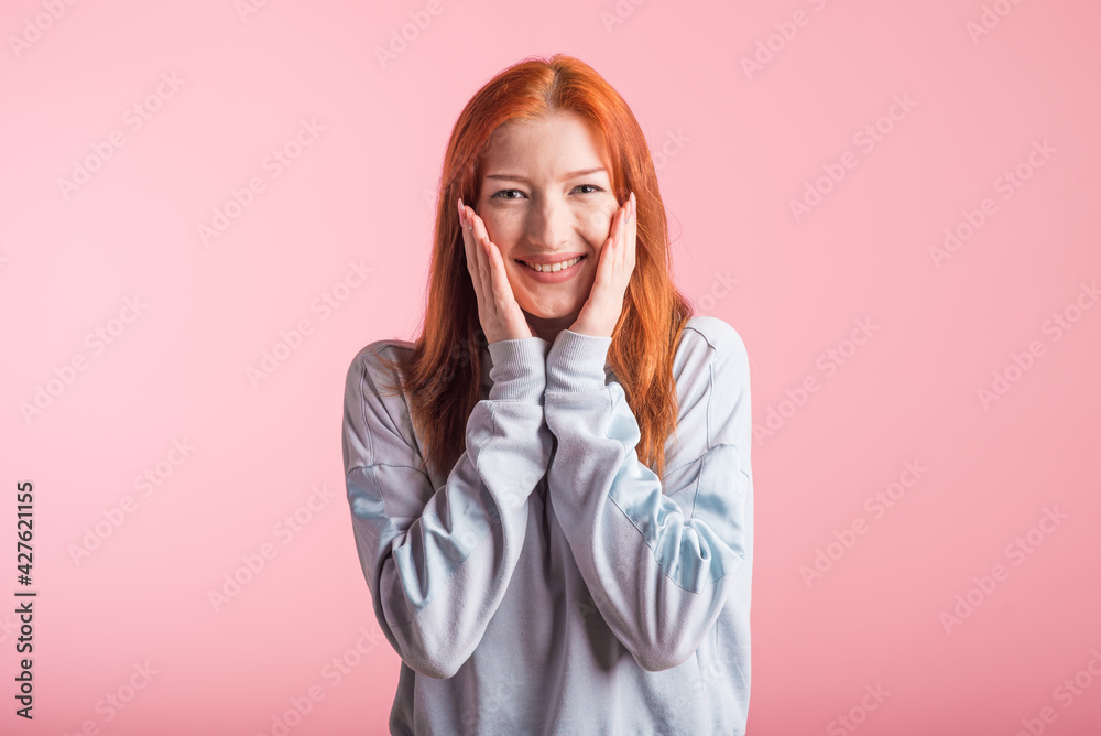 Beautiful young redhead girl in the studio on a pink background