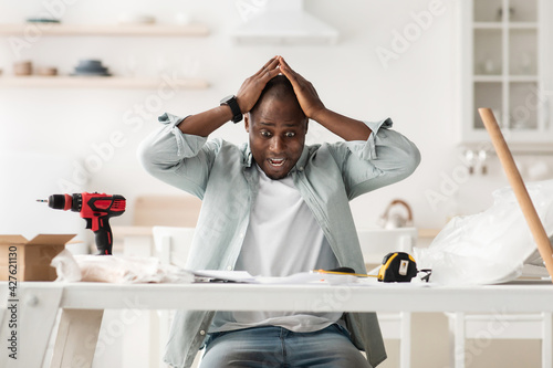 Frightened handyman having problems in assembling new furniture, sitting in kitchen interior