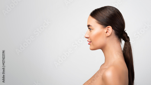 Side-View Portrait Of Young Shirtless Woman Looking Aside, Gray Background