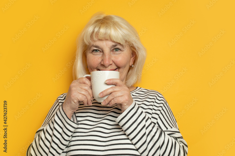 Cheerful young blonde haired woman enjoying drinking tea or coffee on a yellow background Cheerful young blonde haired woman enjoying drinking tea or coffee on a yellow background