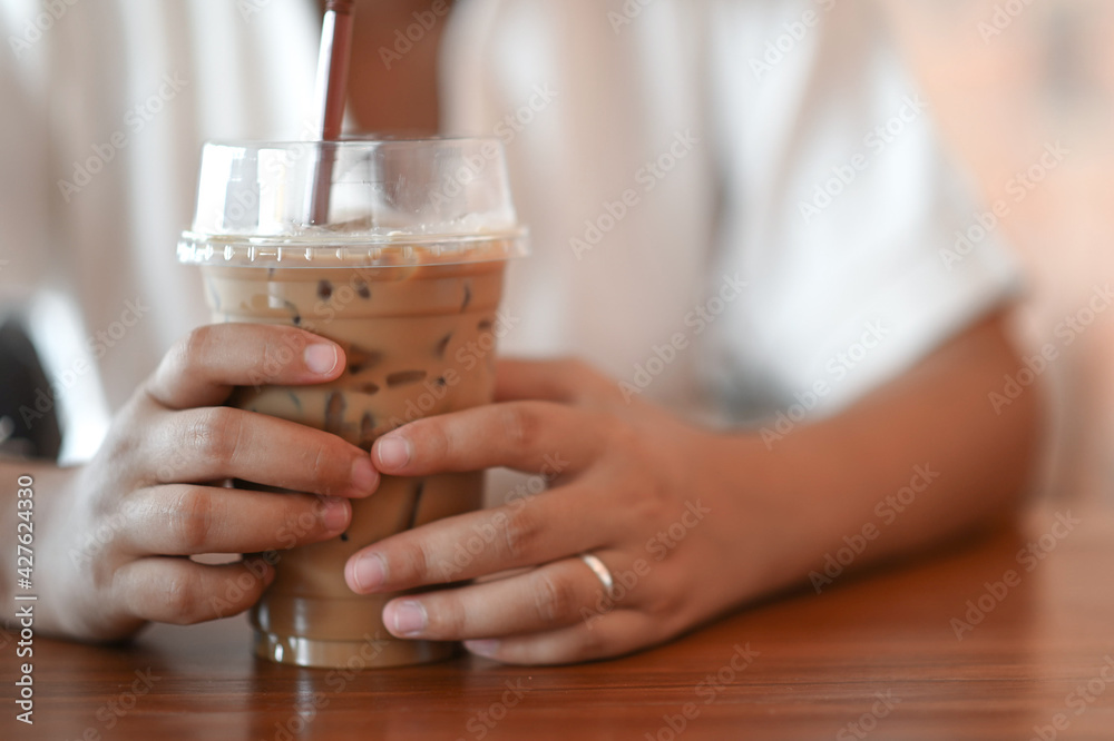 A woman grabbing iced coffee with both hands in the coffee shop.
